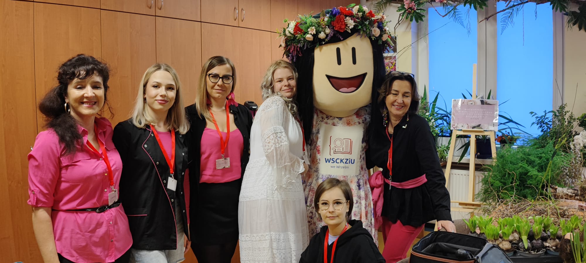 Na fotografii widniej kostium reklamowy w postaci dziewczyny wykreowanej jako lalka pozujący do fotografii z kilkoma uroczymi paniami